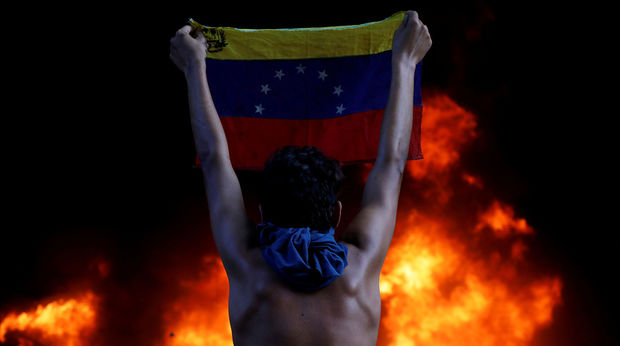 A protestor holds a national flag while standing in front of a fire burning at the entrance of a building housing the magistracy of the Supreme Court of Justice and a bank branch, during a rally against Venezuela's President Nicolas Maduro, in Caracas, Venezuela, June 12, 2017. Protesters angry at the pro-government Supreme Court's ruling attacked a branch of the court with petrol bombs. Carlos Garcia Rawlins: "As had happened before, security forces from inside the building repelled the attack, but this time the clashes were more intense. The demonstrators looted and burned a bank branch in the same building, which was later engulfed in smoke and flames. By the end of the day, several protesters were injured and detained." REUTERS/Carlos Garcia Rawlins/File Photo  SEARCH "POY VENEZUELA" FOR THIS STORY. SEARCH "REUTERS POY" FOR ALL BEST OF 2017 PACKAGES.  TPX IMAGES OF THE DAY. - RC12E26E3310